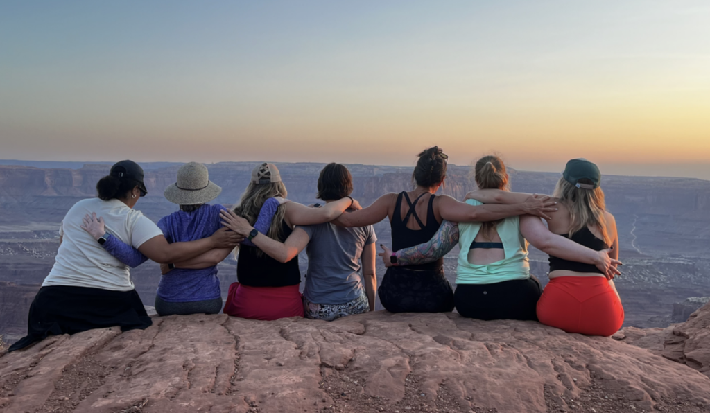 A group of women sitting on a cliff's edge at sunset.